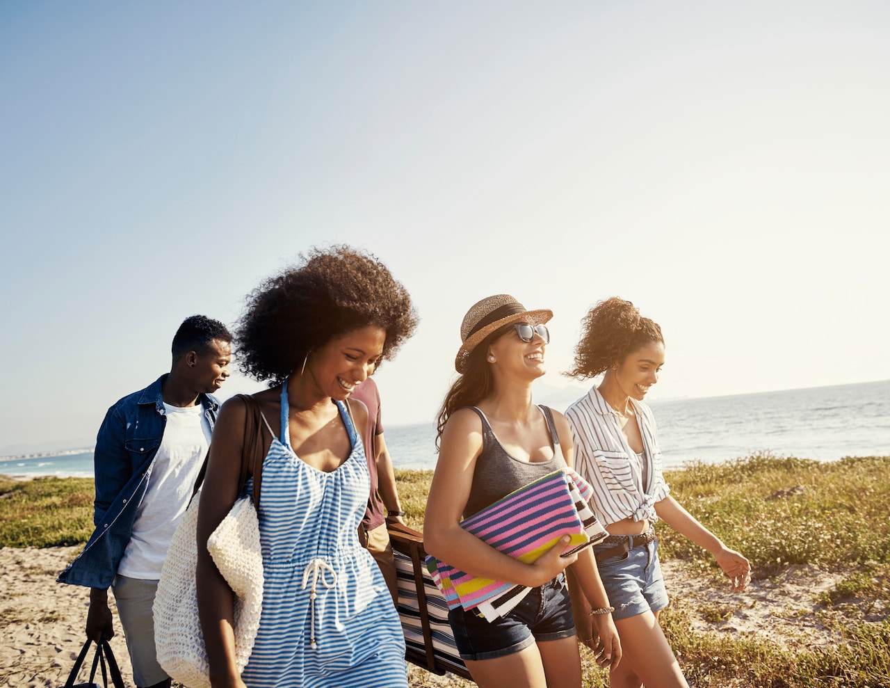3 people with beach gear walking and smiling along beach
